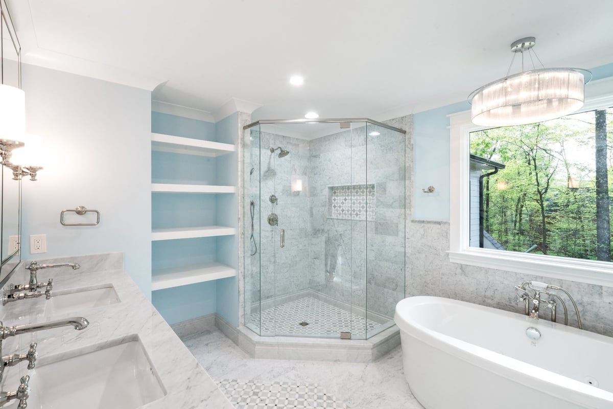 luxury primary bathroom with marble tile glass shower freestanding tub and blue walls in a custom home in charlotte nc