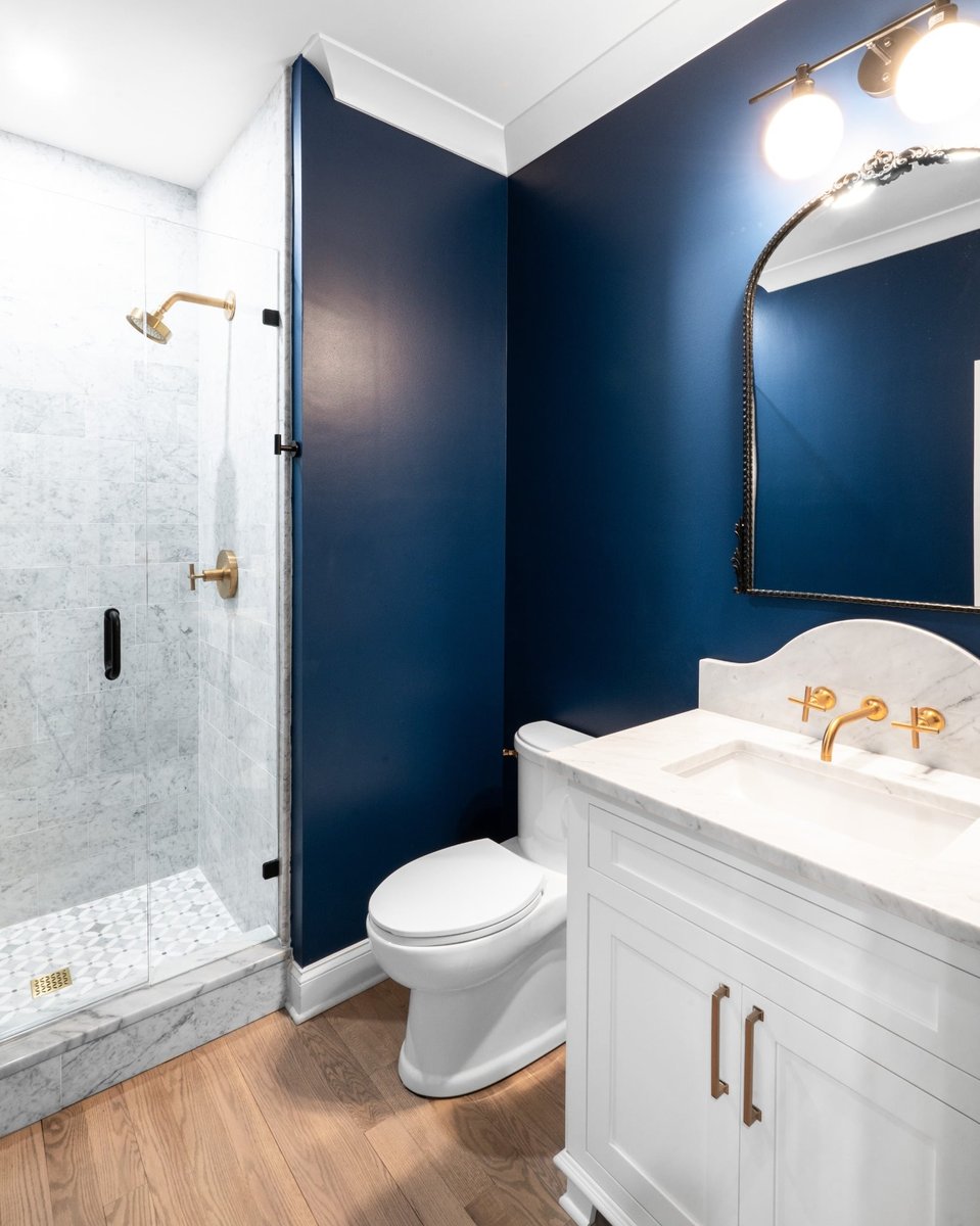 navy blue bathroom with marble shower white vanity and brass fixtures in a custom home in charlotte nc