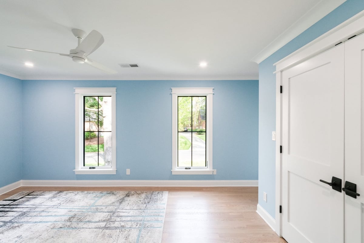 spacious blue bedroom with tall black grid windows and white double doors in a custom home in charlotte nc
