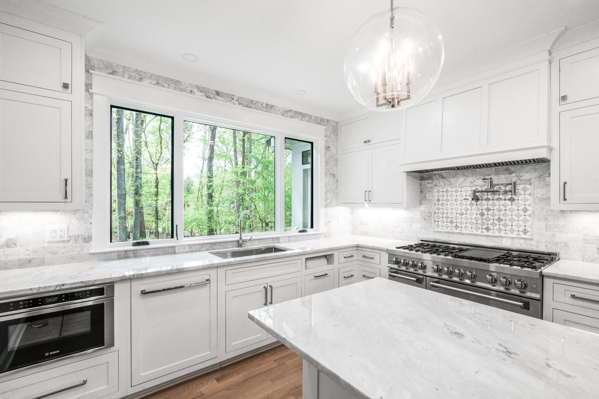 white kitchen with marble countertops large window and stainless steel range in a custom home in charlotte nc