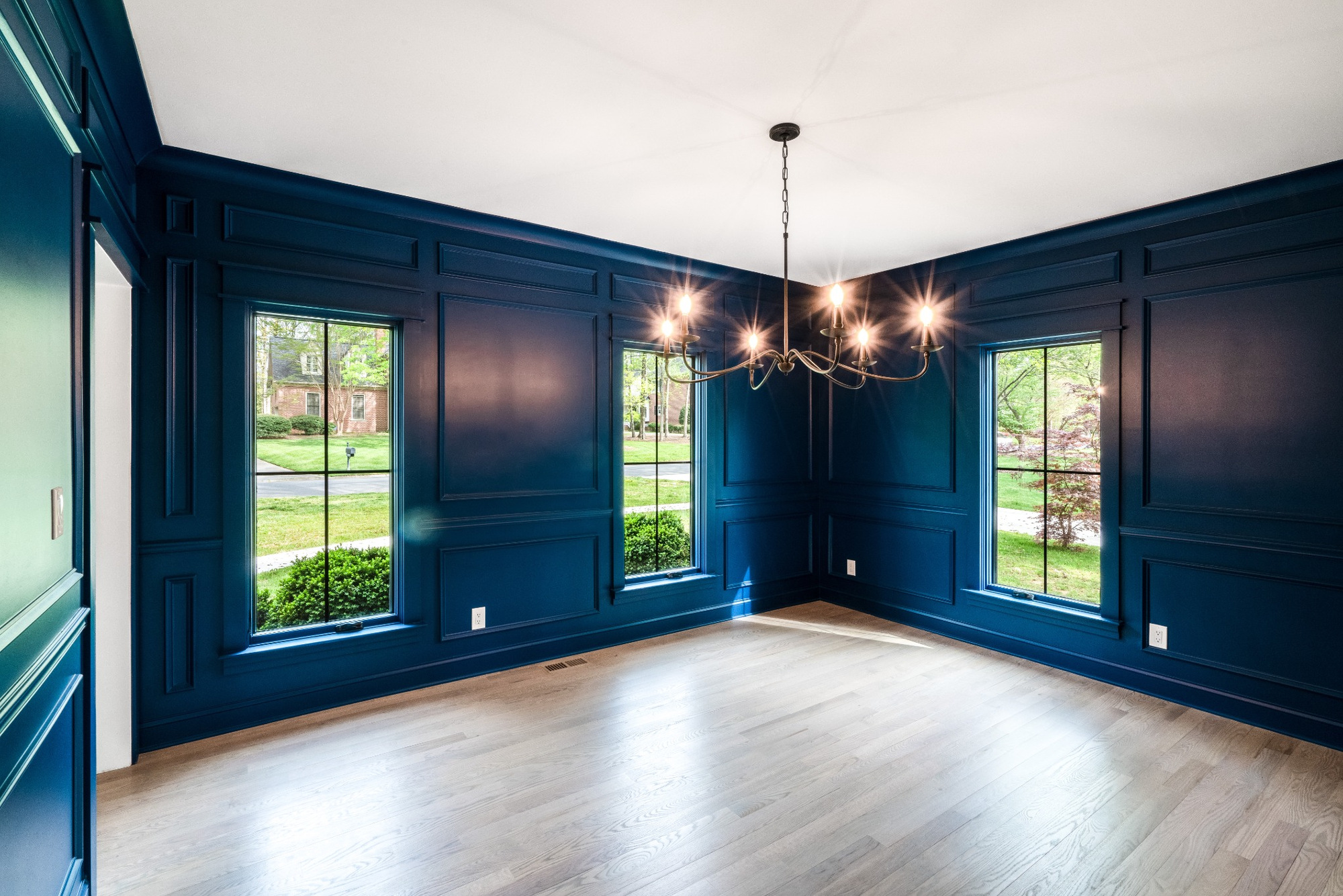 formal dining room with deep blue paneled walls hardwood floors and chandelier in a custom home in charlotte nc